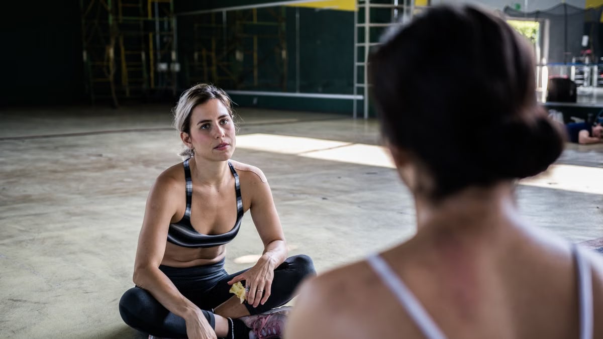 Two women in a workout session, sitting on the gym floor, focused and relaxed.